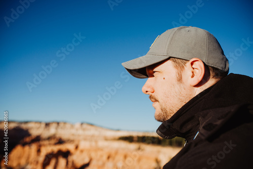 Middle-aged man viewing at Bryce Canyon Nation Park during sunrise, tourist wearing hat and jacket in sunlight, blue sky with copy space in background