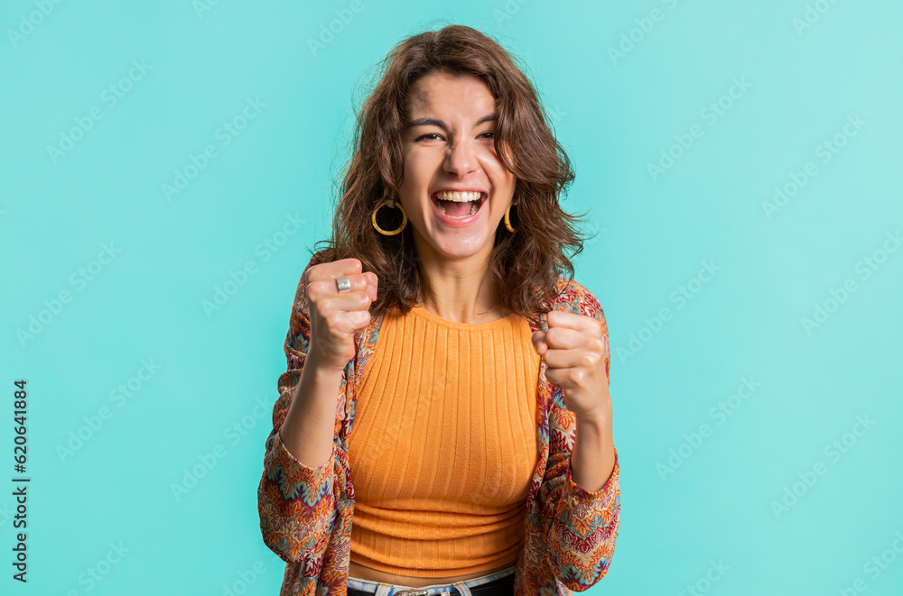 Happy joyful woman shouting, raising fists in gesture I did it, celebrating success, winning, birthday, lottery jackpot goal achievemen, good news. Young brunette girl on blue studio wall background Happy joyful woman shouting, raising fists in gesture I did it, celebrating success, winning, birthday, lottery jackpot goal achievemen, good news. Young brunette girl on blue studio wall background