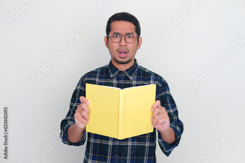 Adult Asian man showing shocked expression while holding a book photo