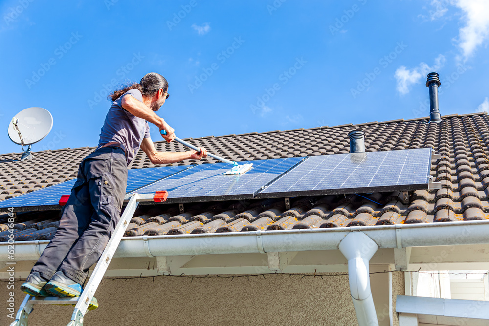 man holding mop cleaning solar panels. cleaning of solar modules with water. close-up of solar panels on the roof on sunny sky. Mop cleaning. Washing of Solar modules in season man holding mop cleaning solar panels. cleaning of solar modules with water. close-up of solar panels on the roof on sunny sky. Mop cleaning. Washing of Solar modules in season