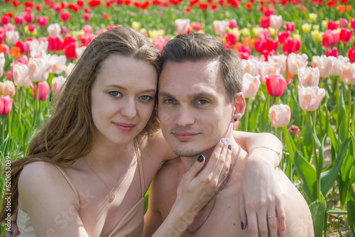 Obraz na płótnie Young beautiful smiling couple sits on the background of a field of colorful tulips. w salonie