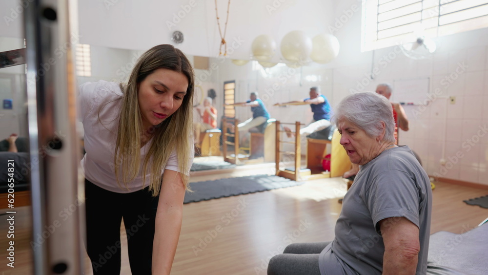 Obraz premium Pilates instructor preparing machine for elderly woman to use, coach prepping equipment for senior person workout routine