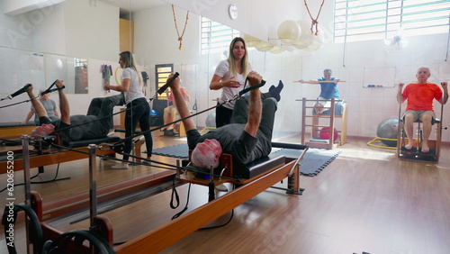Pilates group session of elderly people exercising. Coach orienting a senior man to use workout machine to stretch and strengthen body