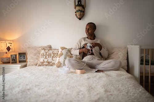 Positive black mom pumping milk in bedroom photo