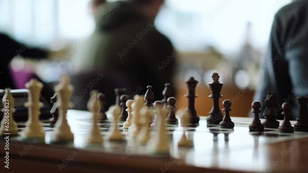 Close-up of Chess Pieces on a Chessboard. Two Men playing Chess Game, Chess Clock. Man Moving a Black Piece Close-up of Chess Pieces on a Chessboard. Two Men playing Chess Game, Chess Clock. Man Moving a Black Piece