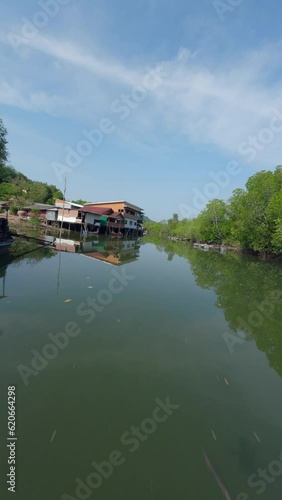 Vertical video. Flying close Asian village embankment boat calm water river local rural house green forest aerial view. FPV sport drone close low shot tropical landscape port harbor fishing ship sunny photo