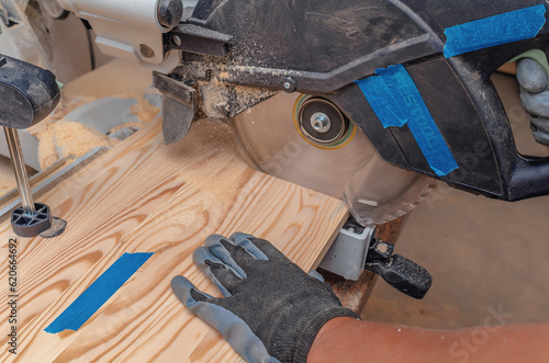 The process of cutting a wooden board with a circular saw. A carpenter's hand in a glove. photo