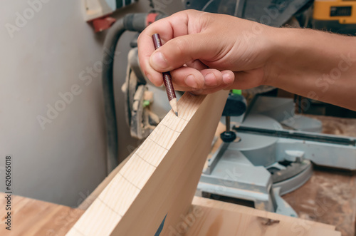 Carpenter's hand writes a marking with a pencil on a wooden board. Design.