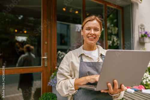 Beautiful flower shop owner wearing apron working on laptop in her store