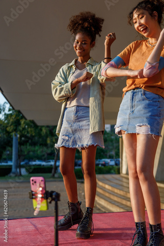 Two women dancing and recording video using mobile phone on street 