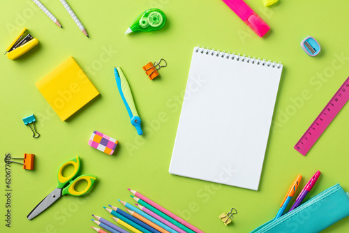 Back to school concept. Flat lay blank paper notepad with school supplies on green background
