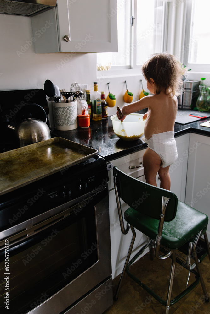 Toddler mixes ingredients while cooking in kitchen Toddler mixes ingredients while cooking in kitchen