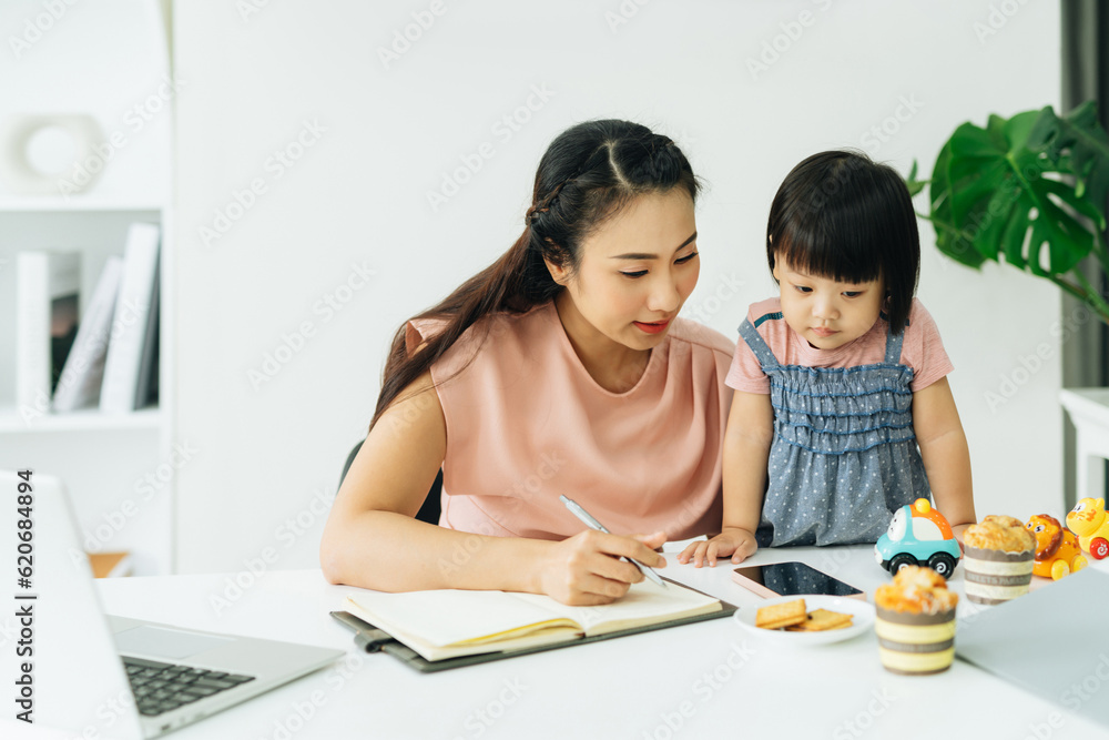 Working mother concept. Young woman working on laptop with her daughte Working mother concept. Young woman working on laptop with her daughte