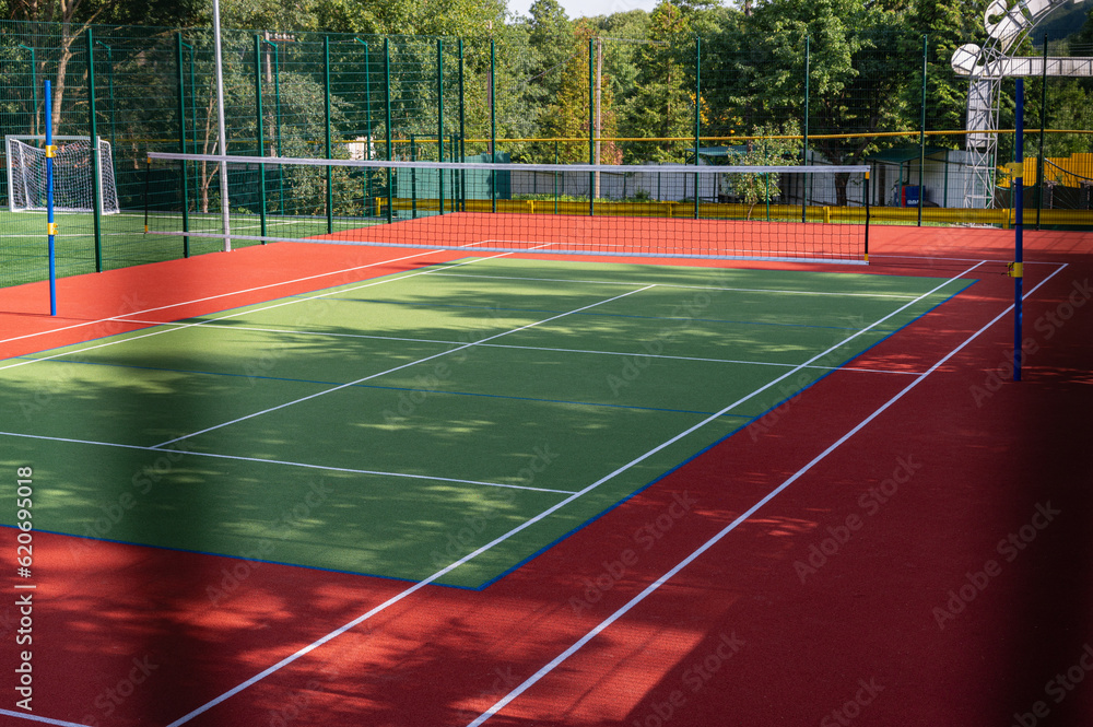 Obraz premium A sports field in a park with artificial grass and a stretched net against the background of green trees, with the morning rays of the sun, at dawn