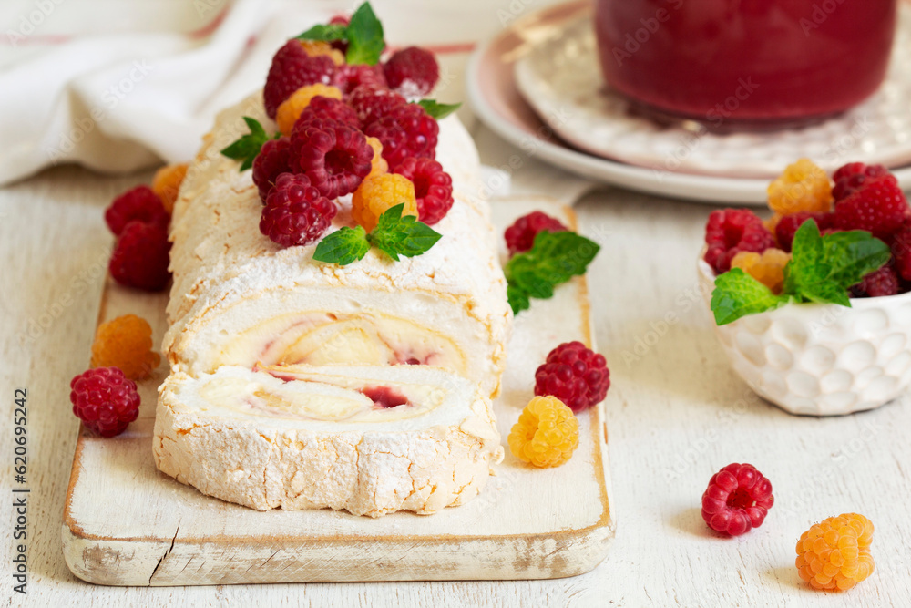 Meringue roll with butter cream and raspberry curd, decorated with berries on a light background.