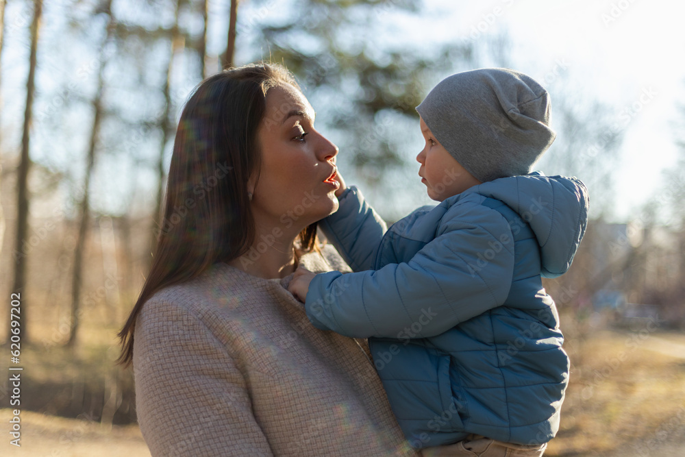 Fototapeta premium Happy family outdoor. Mother embracing her child outdoor. Mom lifting in air little toddler child son. Woman and little baby boy resting walking in park. Mother hugs baby with love care