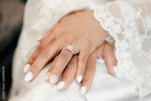 Close-up of a beautiful wedding ring with a precious stone on the bride's finger. Luxurious wedding ring with a large diamond. Bride in white wedding dress with beautiful white manicure