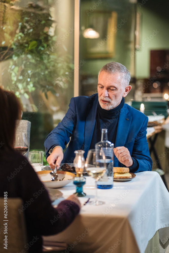 Focused mature man eating meat during date in cafe Focused mature man eating meat during date in cafe