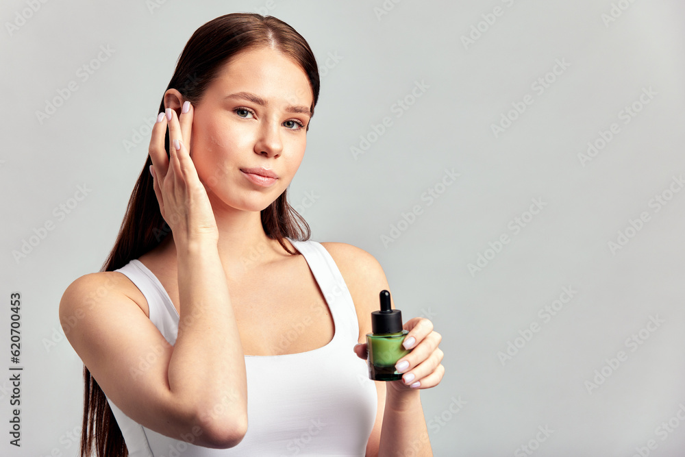 Young attractive girl with long hair applying healing serum on her face. Caucasian woman caring for the skin to maintain her youthful and healthy appearance. Beauty treatment and skincare for women. Young attractive girl with long hair applying healing serum on her face. Caucasian woman caring for the skin to maintain her youthful and healthy appearance. Beauty treatment and skincare for women.