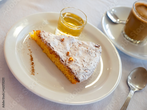 Slice of Spanish almond pie Tarta de Santiago sprinkled with sugar powder accompanied by coffee with milk and glass of sweet wine. Traditional serving of popular dessert