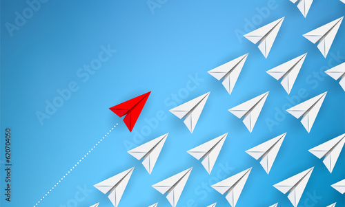 A red paper plane flies alongside a swarm of white paper planes in an attempt to illustrate difference and distinction from others. Copy space