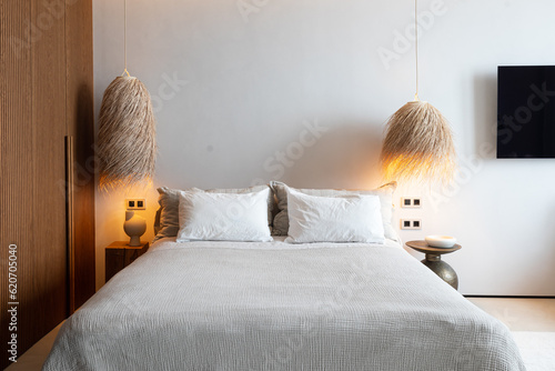 Cozy bed with pillows surrounded by two chandeliers with warm light on photo