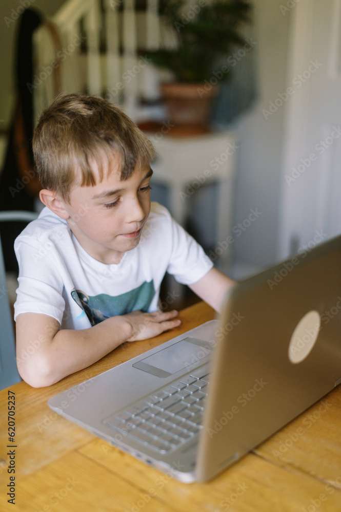 Little kid spending time online and using laptop at kitchen table Little kid spending time online and using laptop at kitchen table