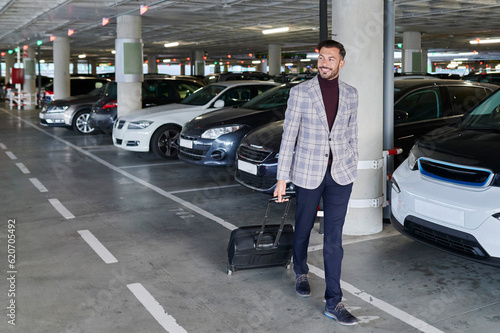 Smiling man walking with luggage in an airport parking lot