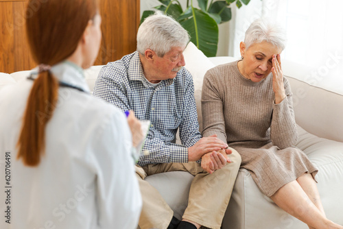 Female doctor examining older senior couple in doctor office or at home. Old woman man patient and doctor have consultation in hospital room. Medicine healthcare medical checkup. Visit to doctor