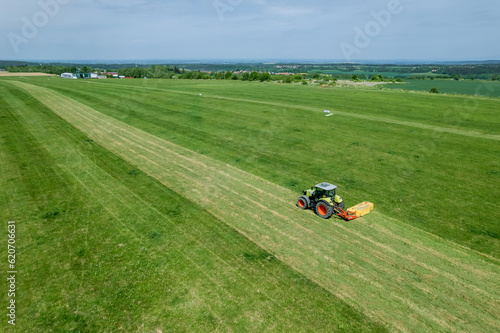 With aid of rotary cutting device, tractor is mowing field. Top view of mowing grass on field.