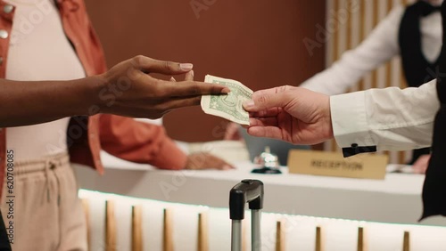 Close up of african american woman handing dollar banknote to bellhop employee after receiving great customer service. Thankful tourist tipping helpful porter for helping with luggage in hotel lobby
