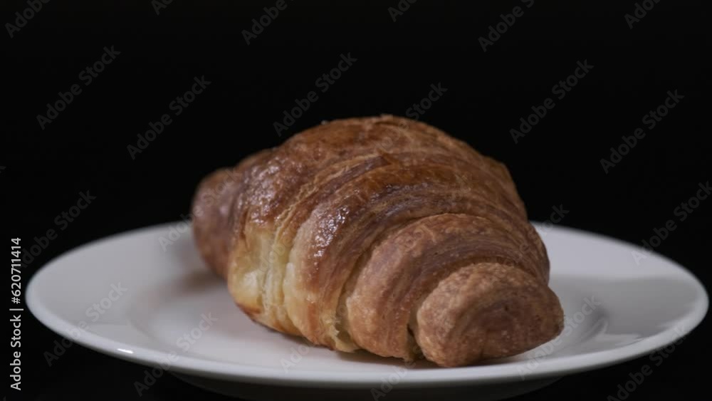 Croissant on white plate rotating in front of camera, Close-up rotates view of Croissant on black background
