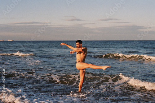 Male ballet dancer posing on the beach at sunset photo