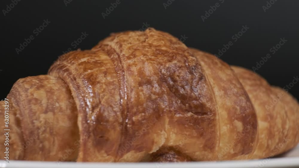 Croissant on white plate rotating in front of camera, Close-up rotates view of Croissant on black background Croissant on white plate rotating in front of camera, Close-up rotates view of Croissant on black background