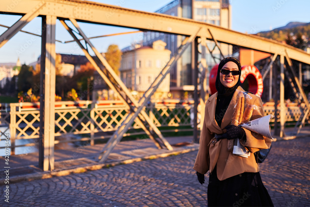 A hijab woman in stylish sunglasses and an elegant French outfit, walking through the city at sunset, carrying a bouquet, bread, and newspaper, radiating a sense of cultural charm and serenity A hijab woman in stylish sunglasses and an elegant French outfit, walking through the city at sunset, carrying a bouquet, bread, and newspaper, radiating a sense of cultural charm and serenity