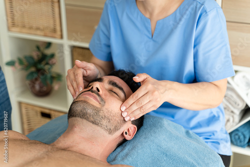 Female masseuse giving relaxing forehead massage to male patient. photo