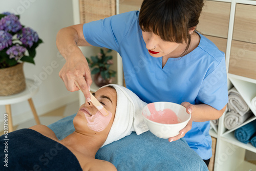 Esthetician applying moisturizing mask to client on a massage table.