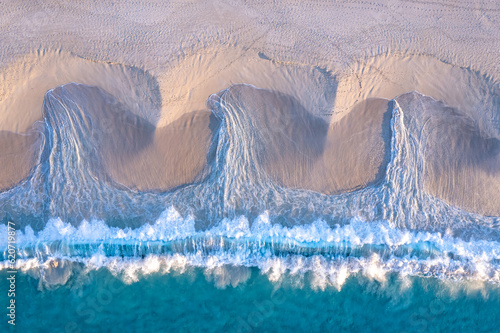 Aerial view of turquoise waves creating patterns in the sand