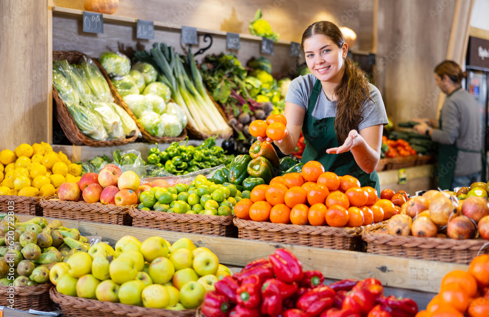 Young woman in apron sells juicy tangerines in greengrocer shop