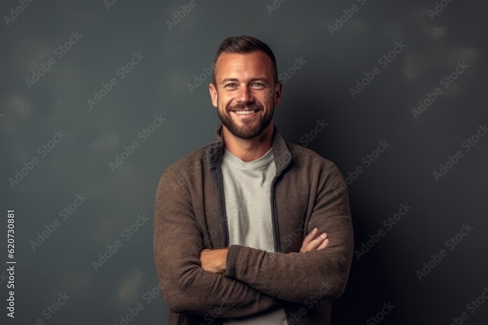 Obraz premium Portrait of a smiling young man standing with arms crossed against grey background