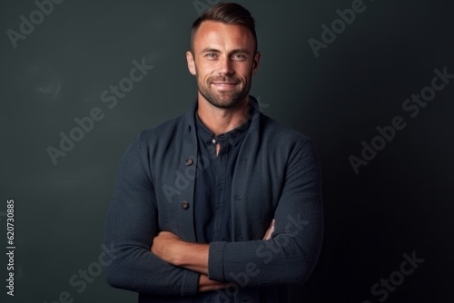 Handsome man standing with crossed arms against chalkboard background.