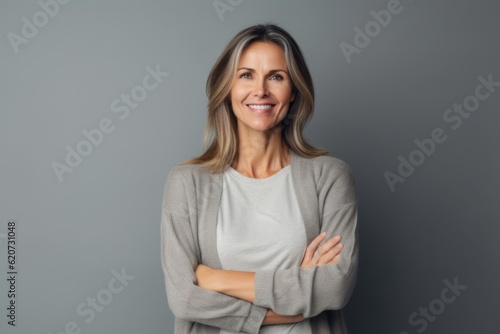Portrait of smiling mature woman with crossed arms standing against grey background
