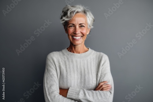 Portrait of smiling senior woman standing with arms crossed against grey background