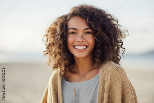 Close up portrait of beautiful young woman with curly hair smiling on the beach