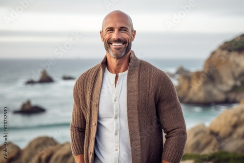 Portrait of smiling mature man standing with hands in pockets at beach