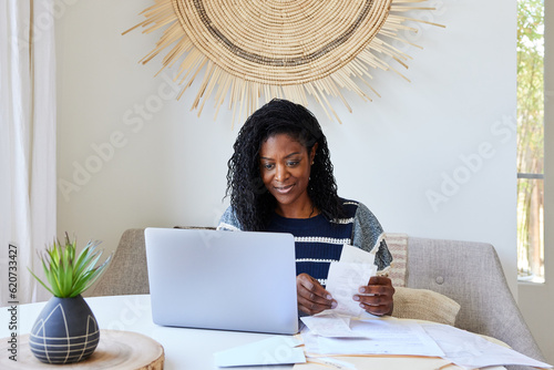 Mature Black woman looking at receipts and finances on computer photo