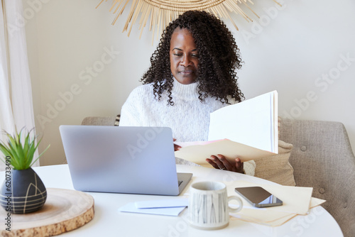 Mature Black woman paying bills online on computer and phone at home photo