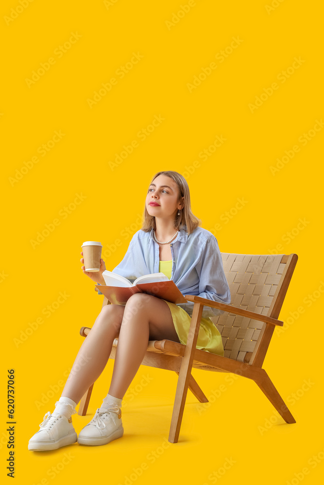 Young woman with cup of coffee and book sitting in wooden armchair on yellow background Young woman with cup of coffee and book sitting in wooden armchair on yellow background