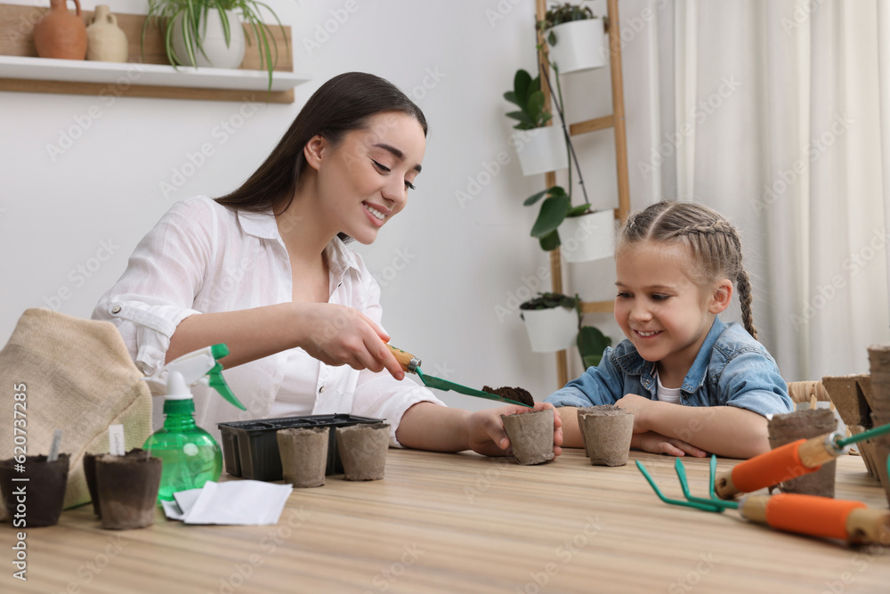 Mother showing her daughter how to fill peat pots with soil at wooden table indoors. Growing vegetable seeds Mother showing her daughter how to fill peat pots with soil at wooden table indoors. Growing vegetable seeds