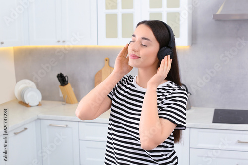 Beautiful woman in headphones enjoying music in kitchen